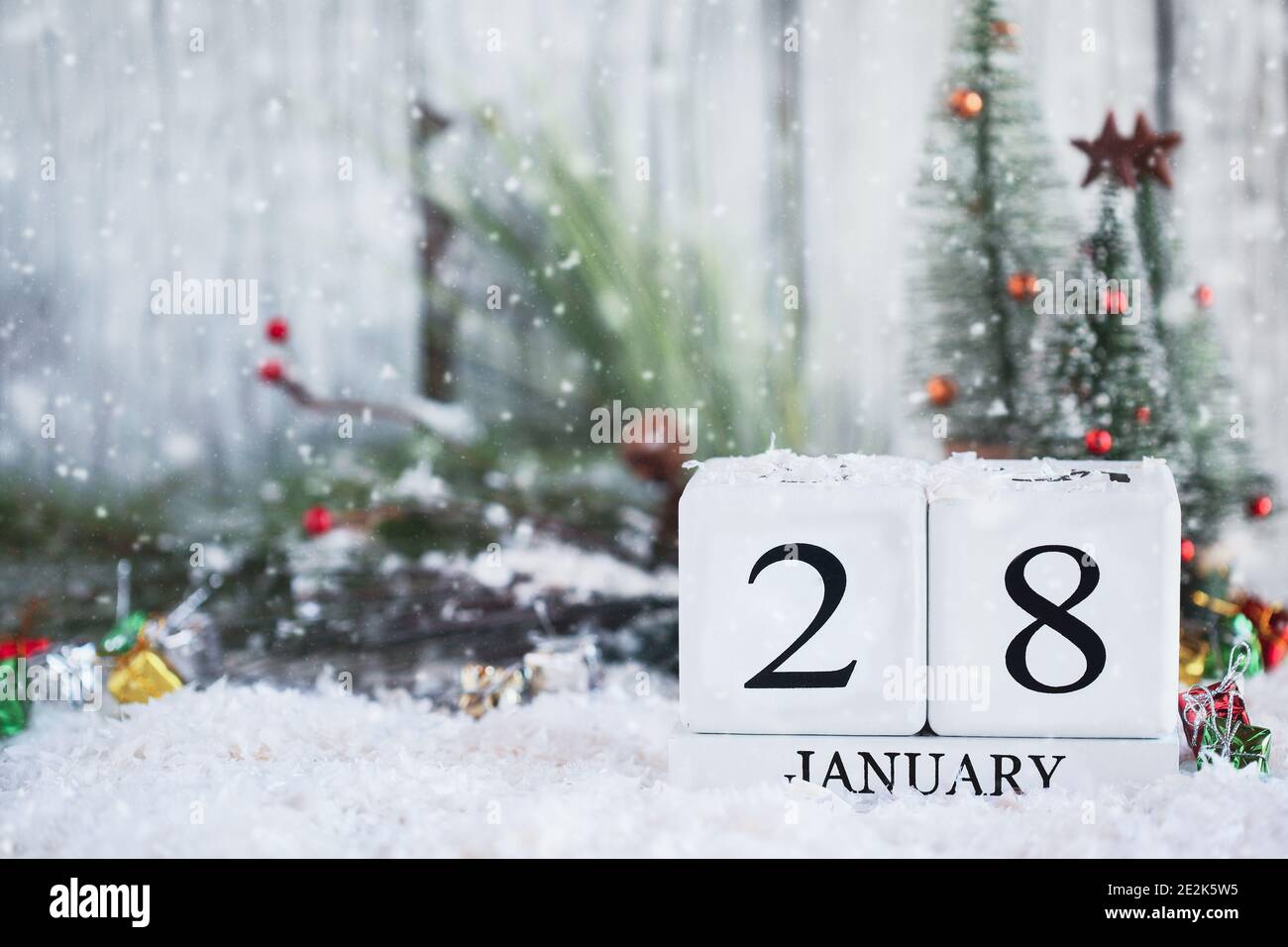 White wood calendar blocks with the date January 28th and Christmas decorations with snow. Selective focus with blurred background. Stock Photo