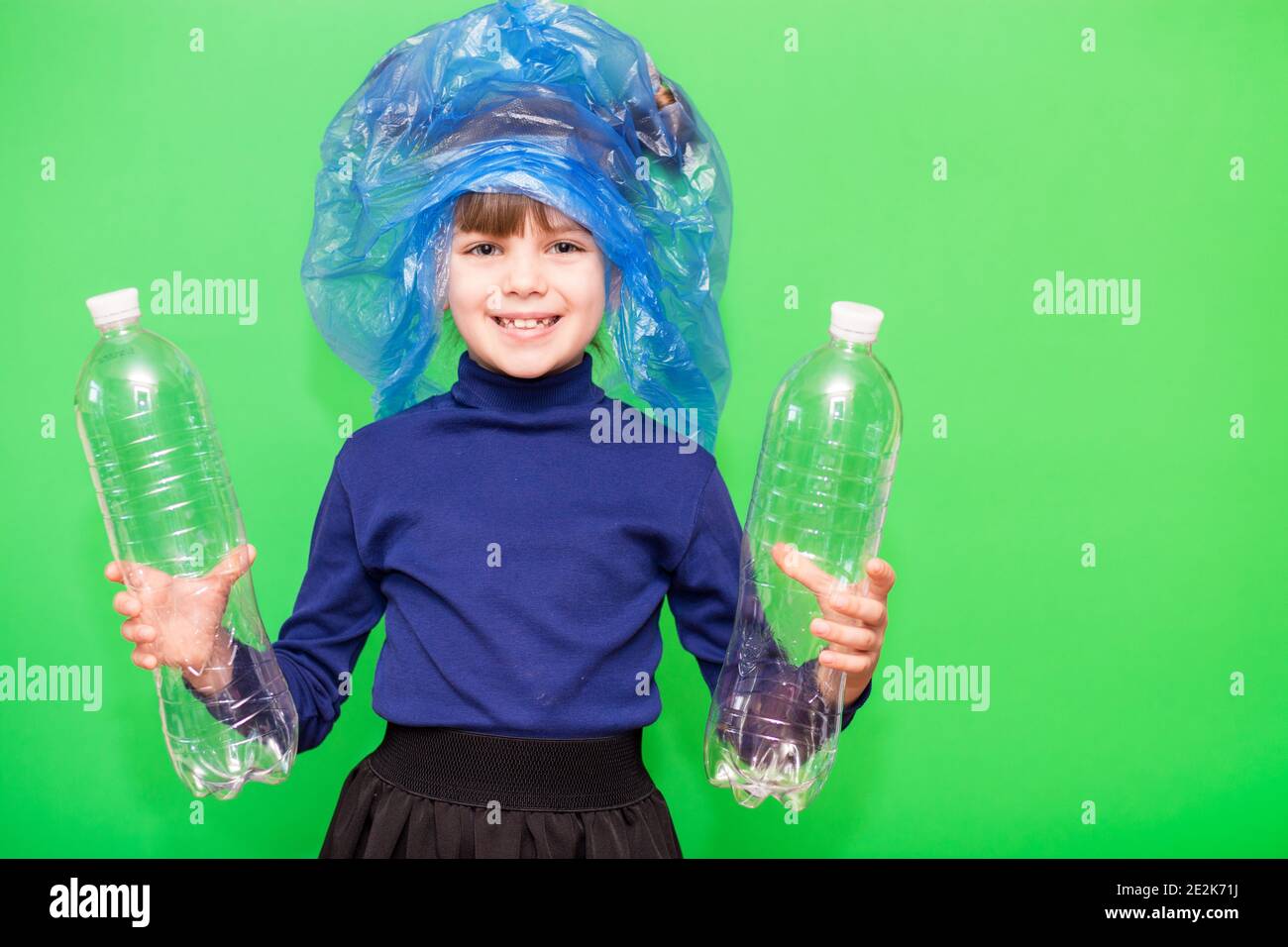 Girl hold trash bag and plastic bottle and shows interest in environmental issues isolated on green background. Child accustomed to bear responsibility for garbage since childhood. Plastic trash sorting concept Stock Photo