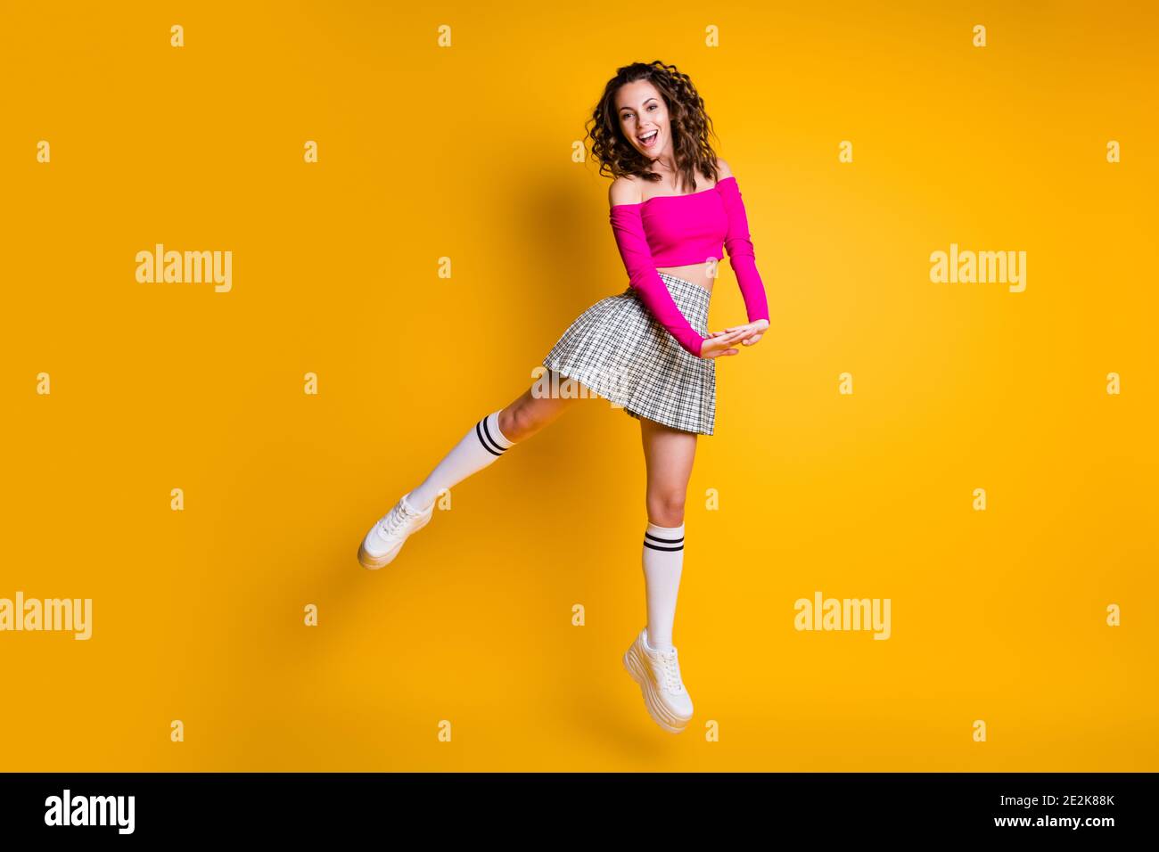 Photo portrait of girl happily jumping up holding hands together wearing pink crop-top plaid skirt knee-high socks white trainers isolated on vivid Stock Photo