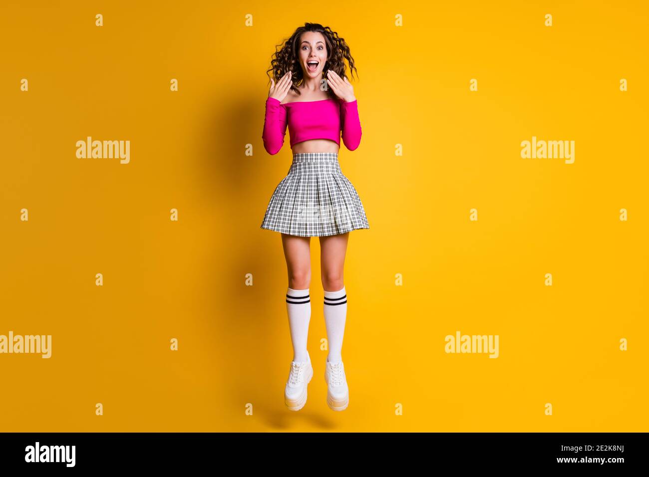 Photo portrait of girl jumping screaming hands near face wearing fuchsia crop-top checkered skirt knee-high socks white sneakers isolated on bright Stock Photo