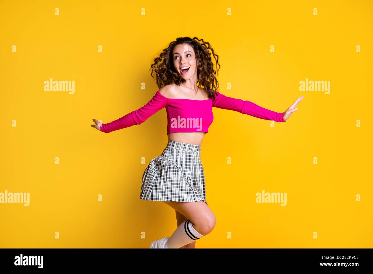 Photo portrait of woman skipping jumping standing on one leg hands to sides open mouth wearing fuchsia crop-top plaid skirt knee-high socks isolated Stock Photo