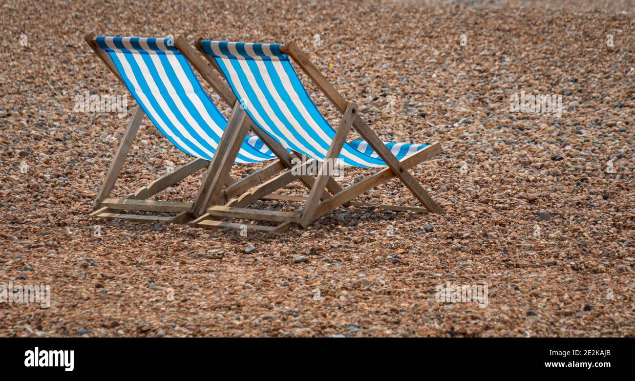 Two blue and white striped deckchairs on a pebble beach Stock Photo - Alamy