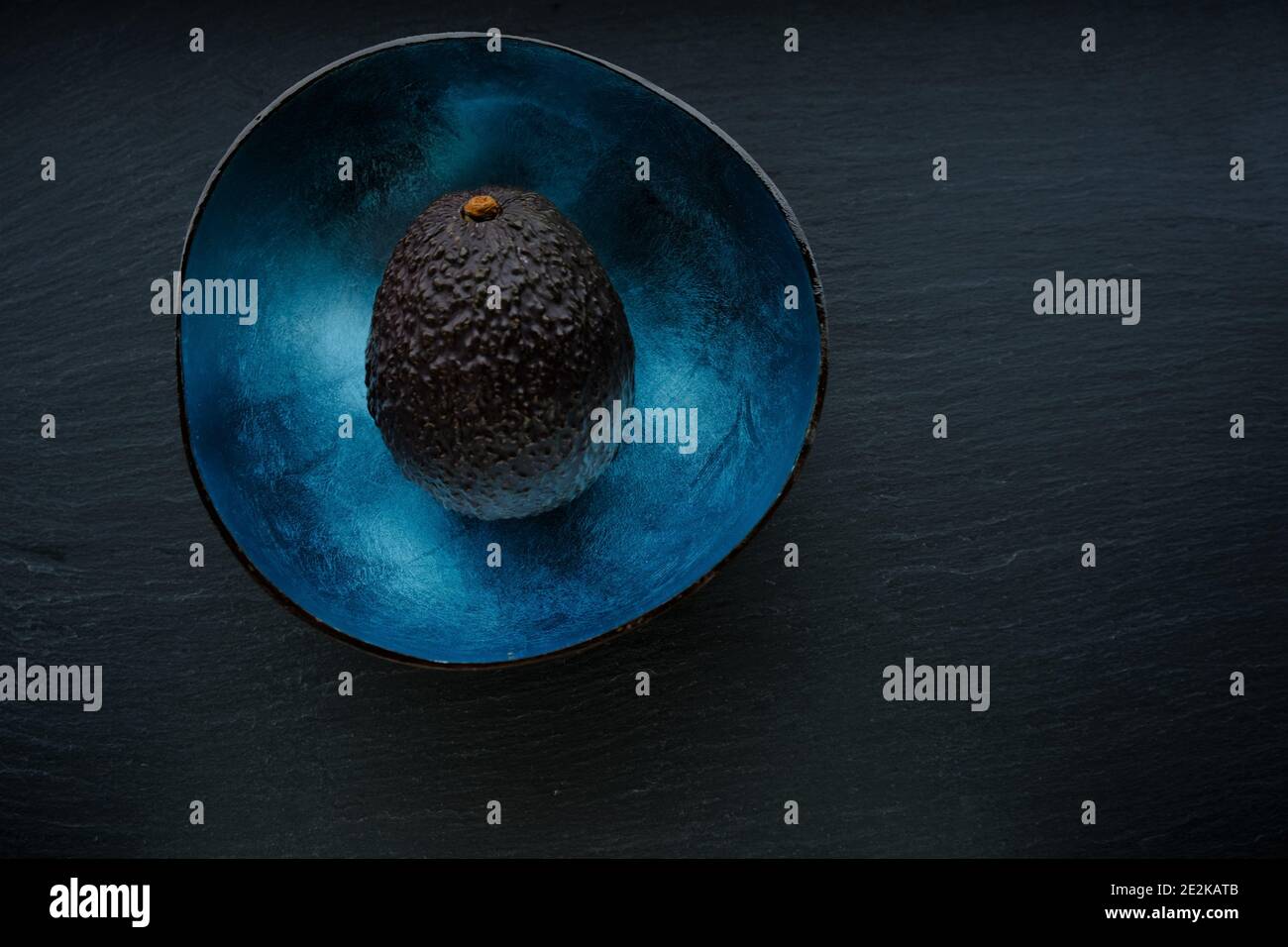 Avocado. brown avocado fruits in a blue cup on a black slate background.Super food. useful food product. Stock Photo