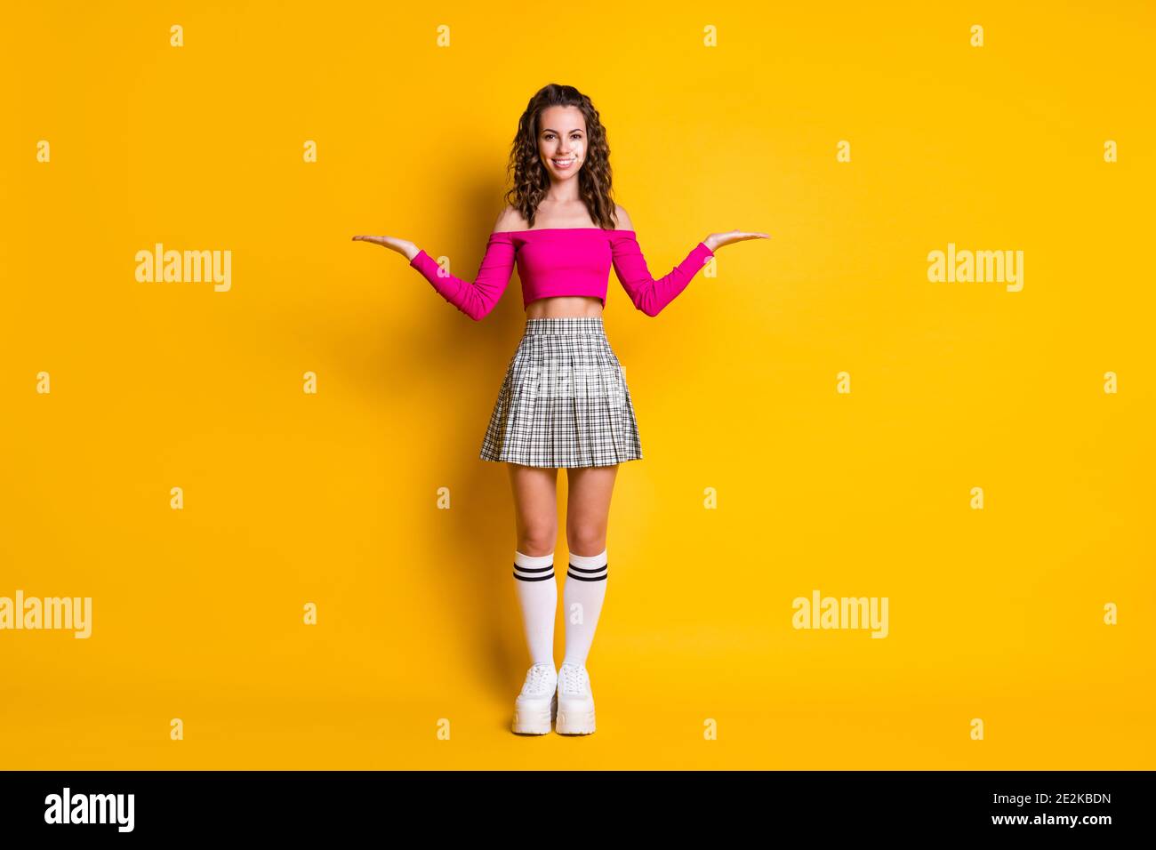 Photo portrait full body view schoolgirl holds hands palms with copyspaces showing choices wearing pink top checkered skirt trainers knee-high socks Stock Photo