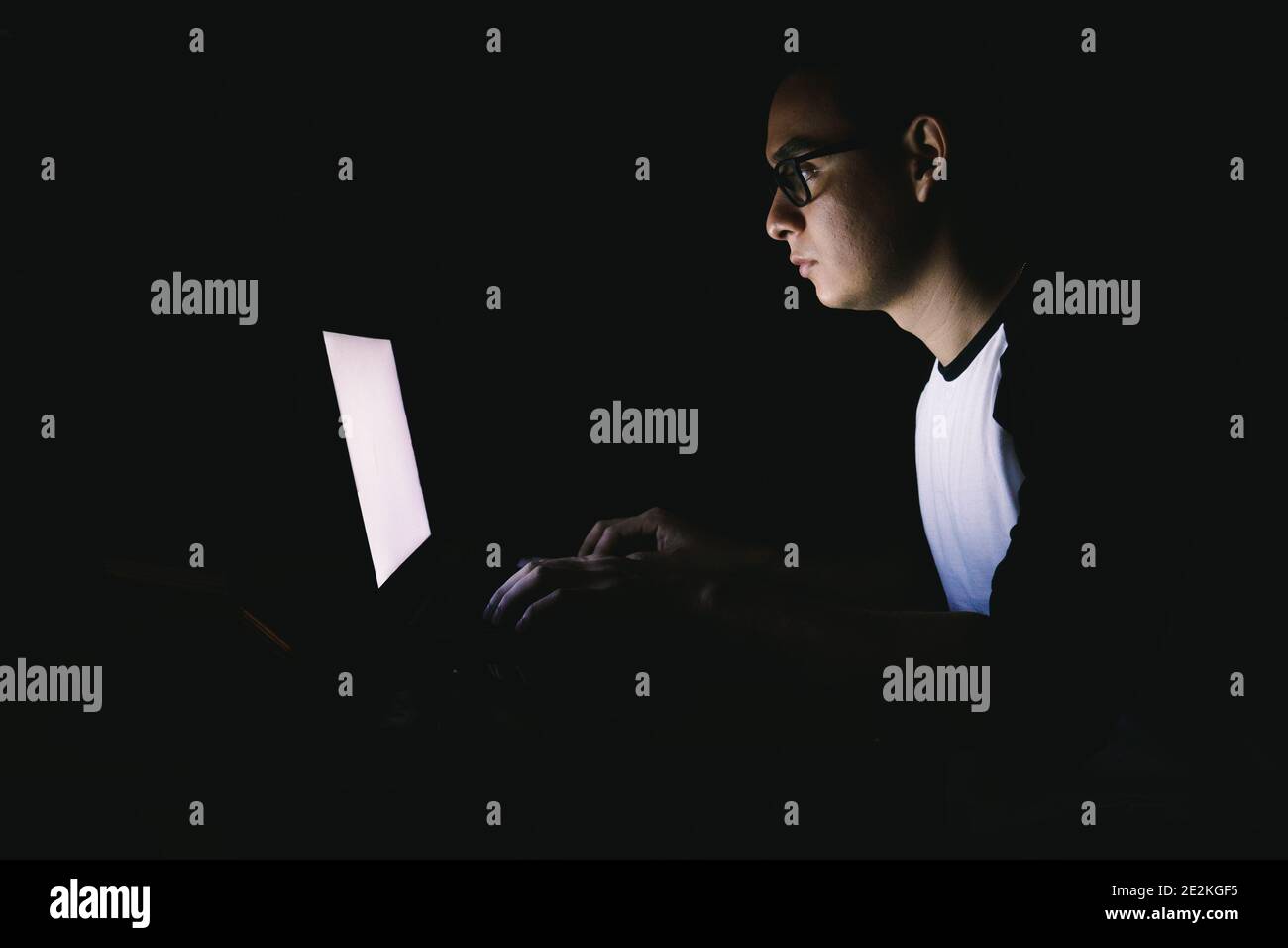 Caucasian workaholic young man working late night from home sitting on a desktop and using his laptop Stock Photo