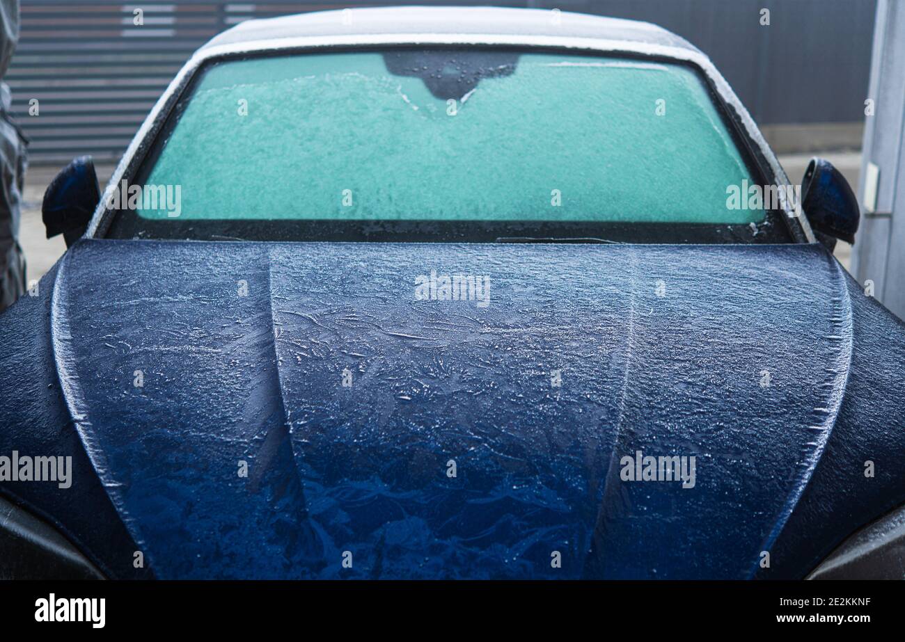 Modern Blue Body Car Covered in Frost During Freezing Cold Winter Morning. Front of the Vehicle. Seasonal Automotive Maintenance and Weather Elements. Stock Photo