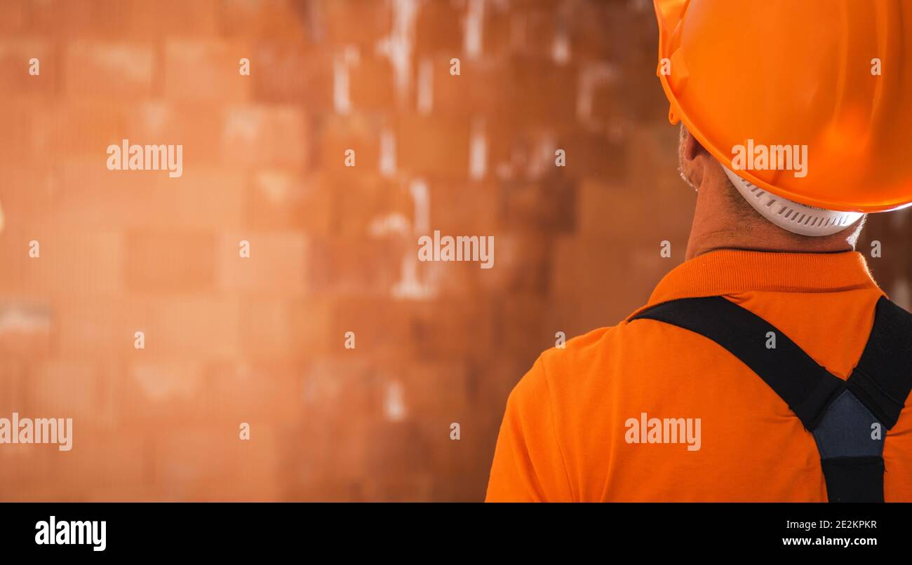 Hard Hat Area Construction Contractor Staying Back to Camera and Looking on the Newly Built Concrete Blocks Made Building. Banner with Left Side Copy Stock Photo