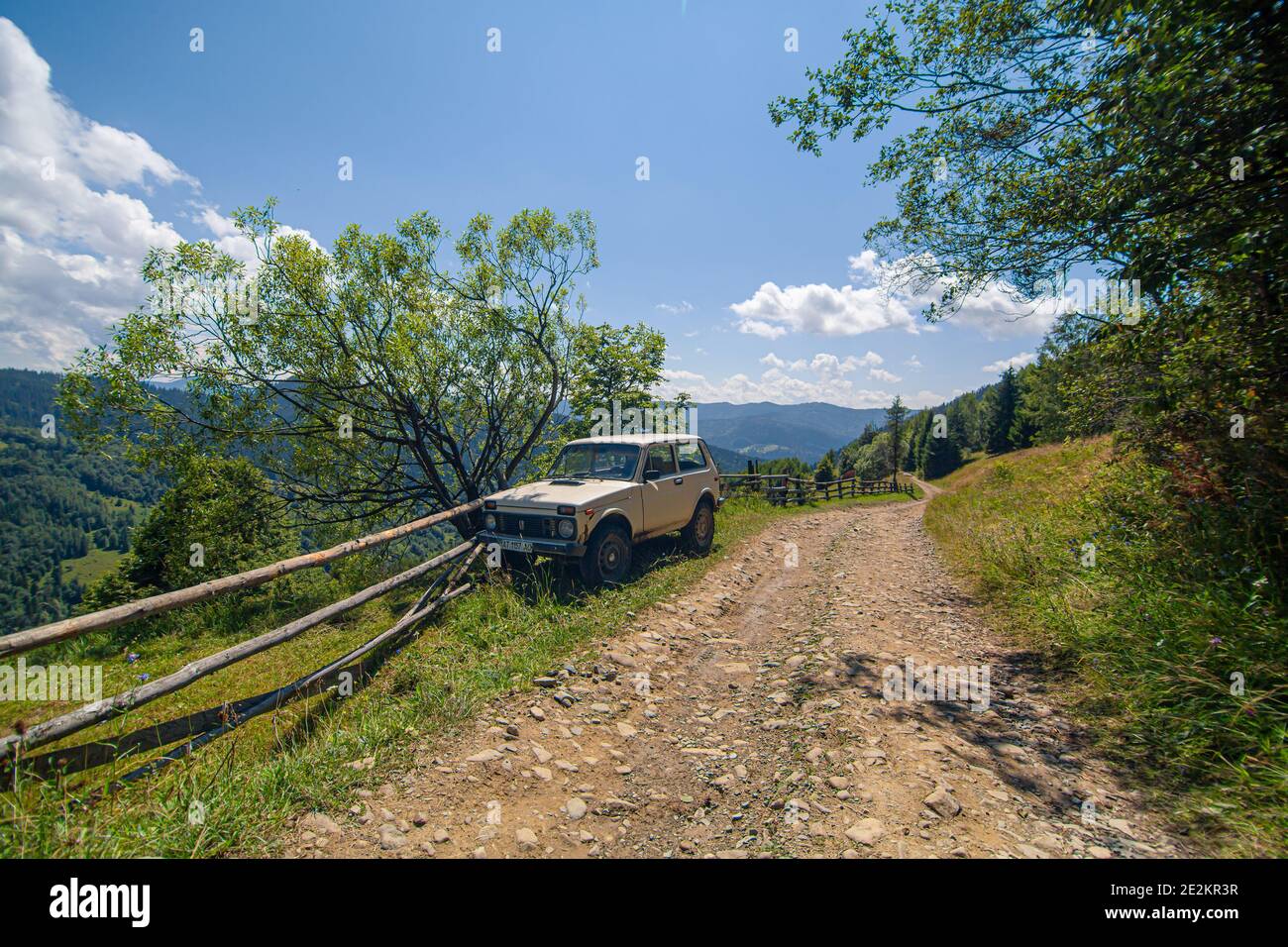 Old russian jeep parked next to wooden fence on the mountain dirty road. Summer day. Mountain tour. Stock Photo