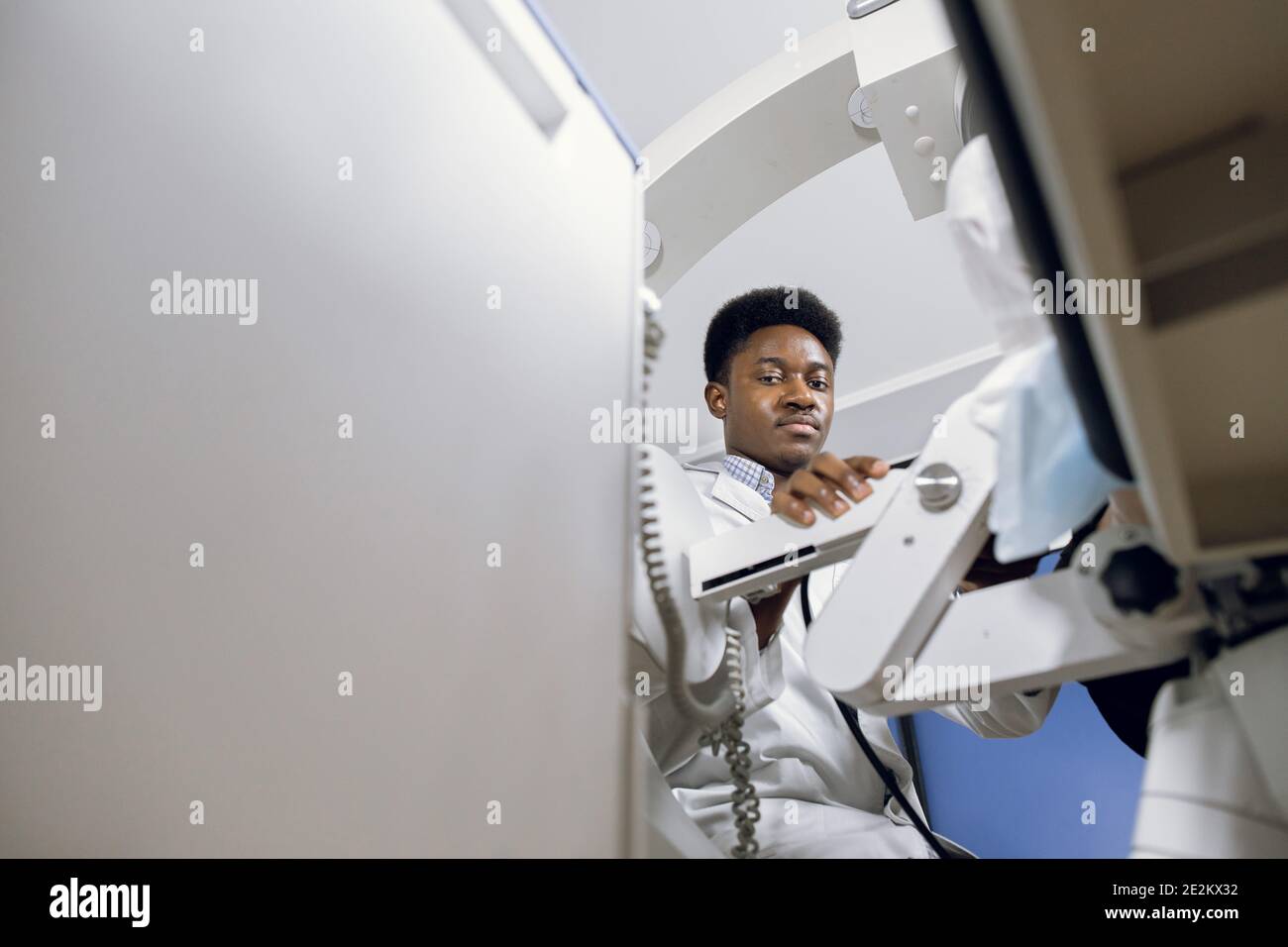 Bottom view of young handsome high-skilled African doctor in white coat, working with modern lithotripter equipment for non-invasive extracorporeal Stock Photo