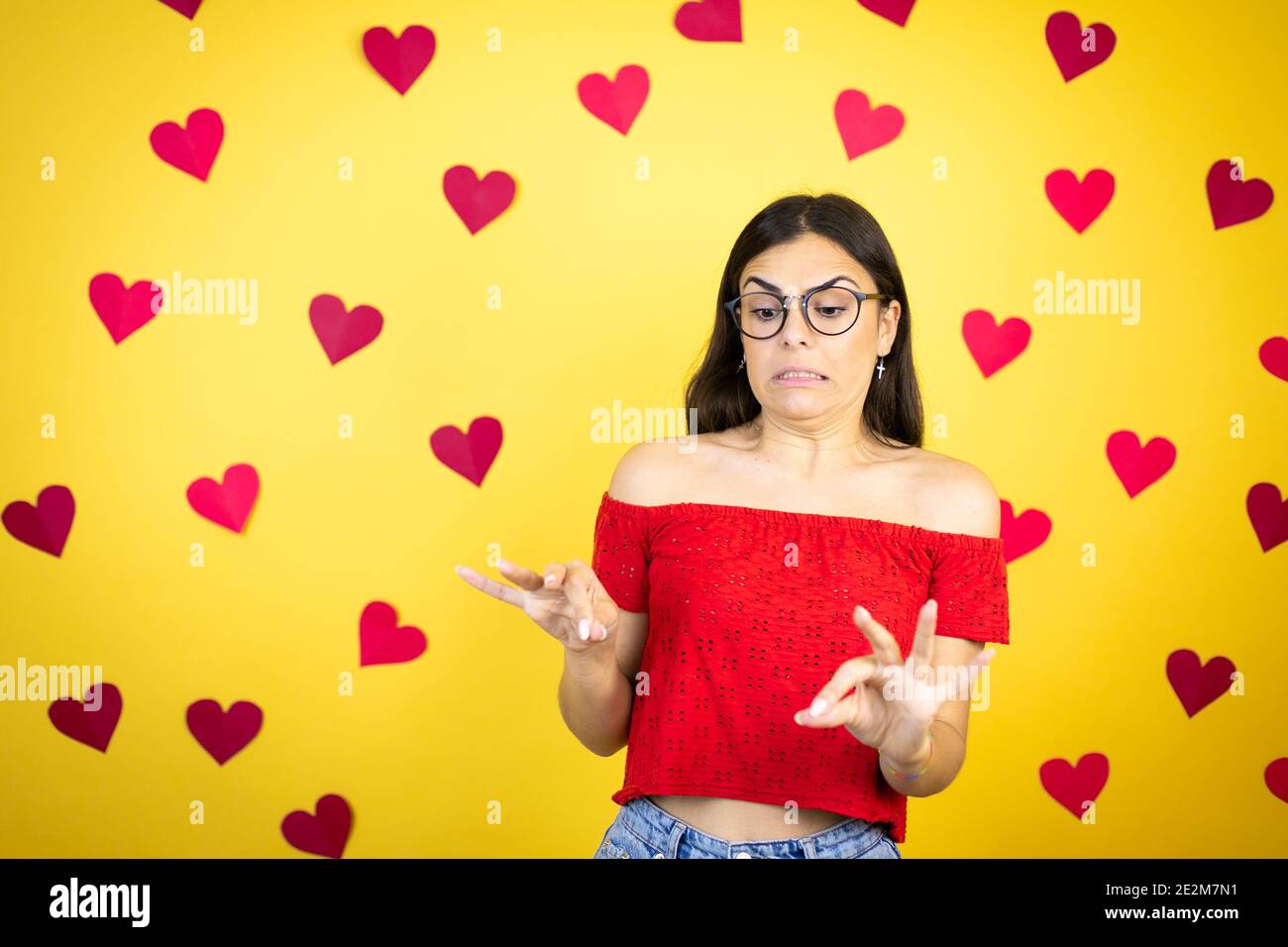 Young beautiful woman over yellow background with red hearts disgusted expression, displeased and fearful doing disgust face because aversion reaction Stock Photo