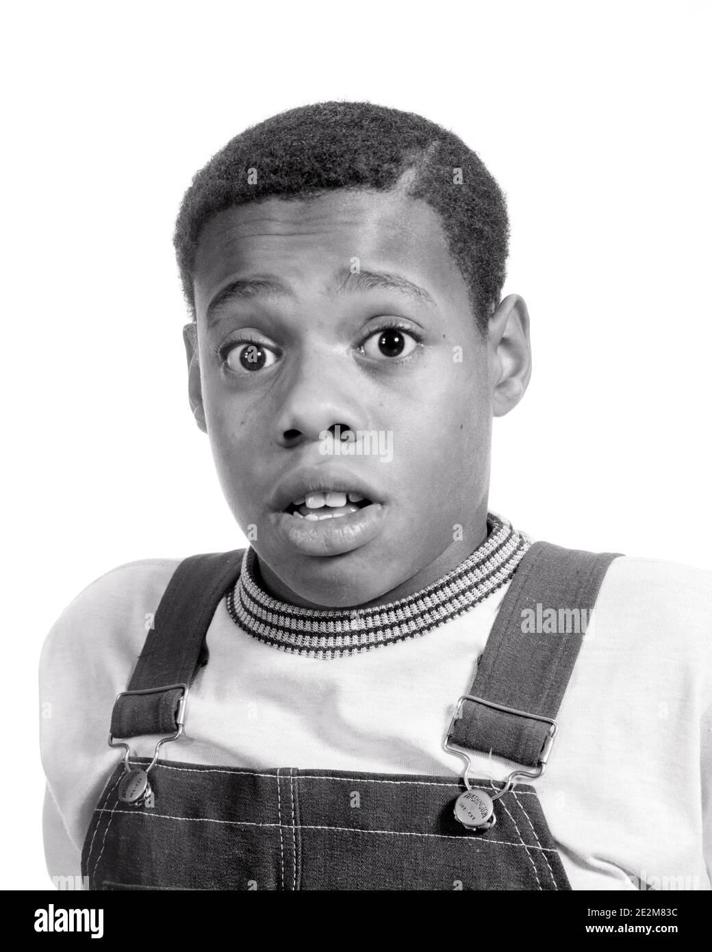1970s SURPRISED FACIAL EXPRESSION AFRICAN-AMERICAN PRE-TEEN BOY WEARING T-SHIRT BIB OVERHAULS WIDE-EYED LOOKING AT CAMERA - b25647 HAR001 HARS EXPRESSIONS B&W EYE CONTACT BUG-EYED HEAD AND SHOULDERS DISCOVERY AFRICAN-AMERICANS AFRICAN-AMERICAN EXCITEMENT BLACK ETHNICITY CONCEPTUAL TEENAGED T-SHIRT WIDE-EYED BIB PRE-TEEN PRE-TEEN BOY STARTLED BLACK AND WHITE HAR001 OLD FASHIONED AFRICAN AMERICANS Stock Photo