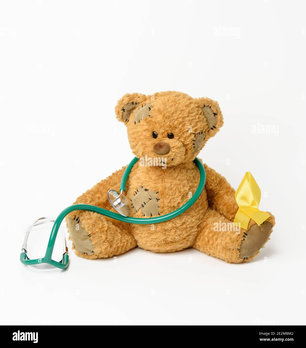 brown teddy bear with a patch, silk yellow ribbon in the shape of a loop on a white background, concept of the fight against childhood cancer, problem Stock Photo