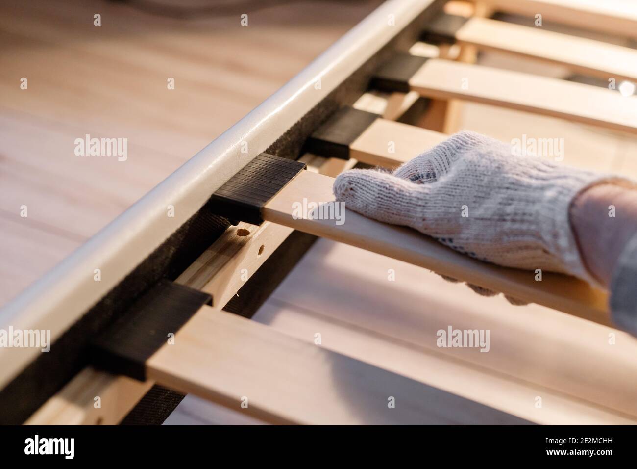 Male worker's hand in glove assembling bed, connecting slats to bed