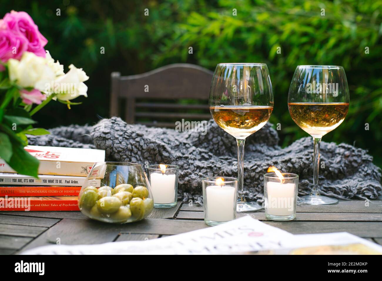Wine, olives and books on wooden table in outdoor garden setting. Cosy home decor, relaxed tablescape. Summertime, laid-back weekend lifestyle in UK Stock Photo
