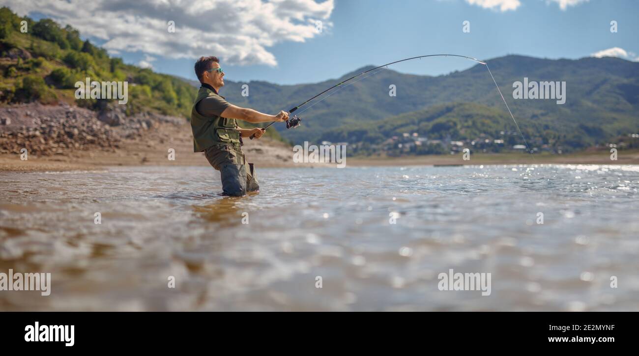 Fisherman pulling a fish with a fishing rod on a lake in Mavrovo, Macedonia Stock Photo
