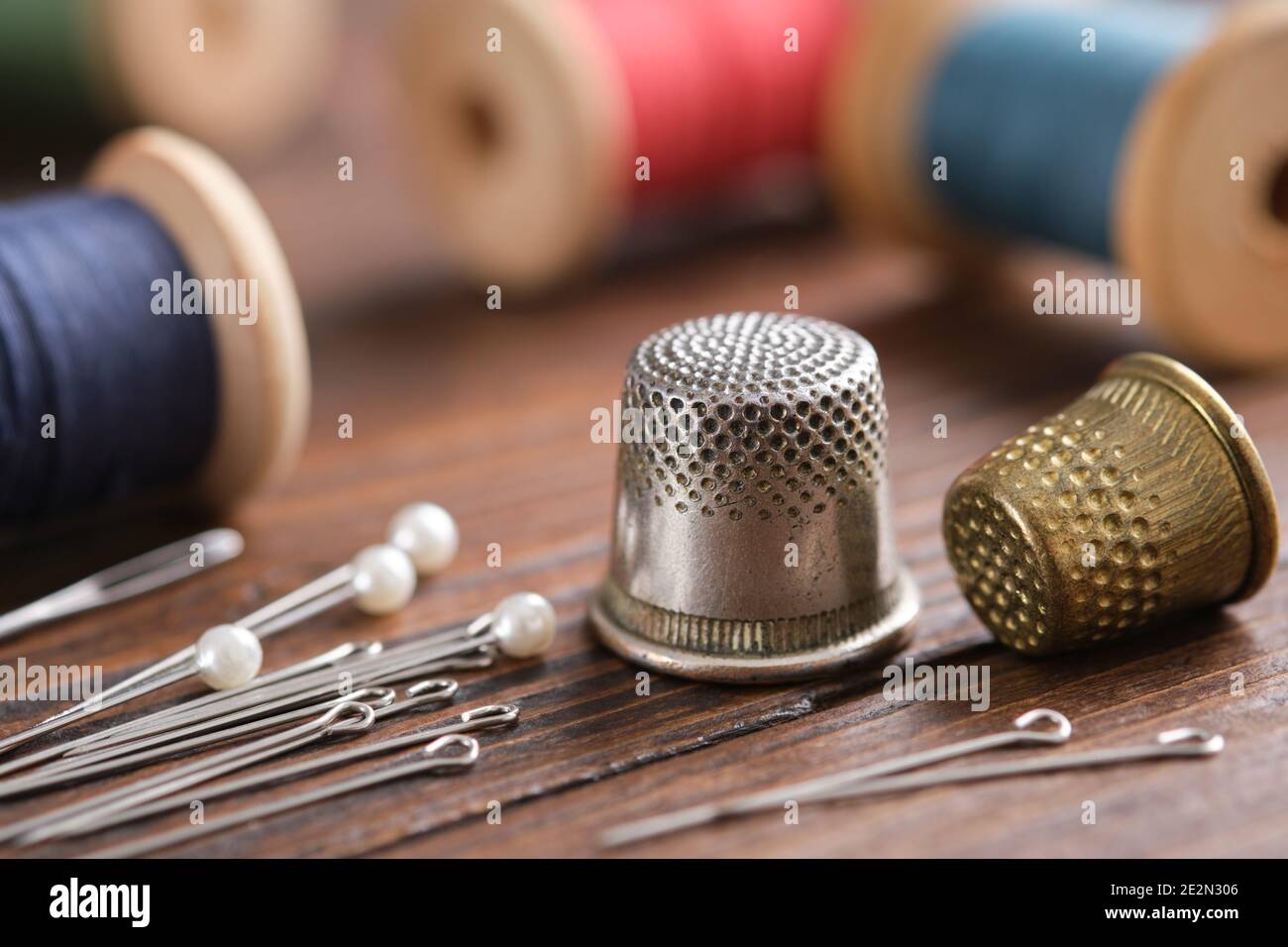 Two thimbles and including pins. Various wooden spools of multicolored threads on background. Stock Photo