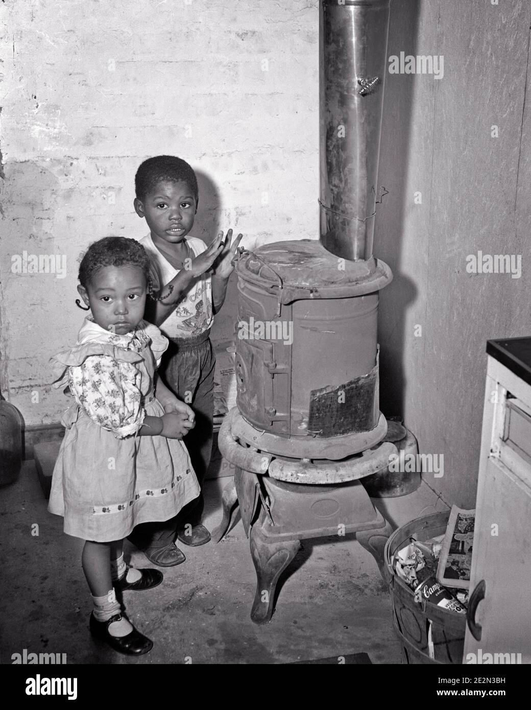 1950s 1960s TWO YOUNG AFRICAN AMERICAN CHILDREN BOY GIRL LOOKING AT CAMERA KEEPING WARM BY CAST IRON STOVE POOR WELFARE HOUSING - n536 HAR001 HARS OLD FASHION SISTER POVERTY 1 JUVENILE COAL LIFESTYLE FEMALES BROTHERS POOR RURAL HOME LIFE COPY SPACE HALF-LENGTH RESIDENTIAL MALES FUEL WARM SIBLINGS SISTERS B&W SADNESS EYE CONTACT HIGH ANGLE DANGEROUS WELFARE AFRICAN-AMERICANS AFRICAN-AMERICAN BLACK ETHNICITY BY HOMES SIBLING CONCEPTUAL WARMTH RESIDENCE DISADVANTAGED BABY BOY COOPERATION DISAFFECTED DISAPPOINTED DISCONNECTED GROWTH IMPOVERISHED JUVENILES KEEPING MISERABLE NEED TOGETHERNESS Stock Photo