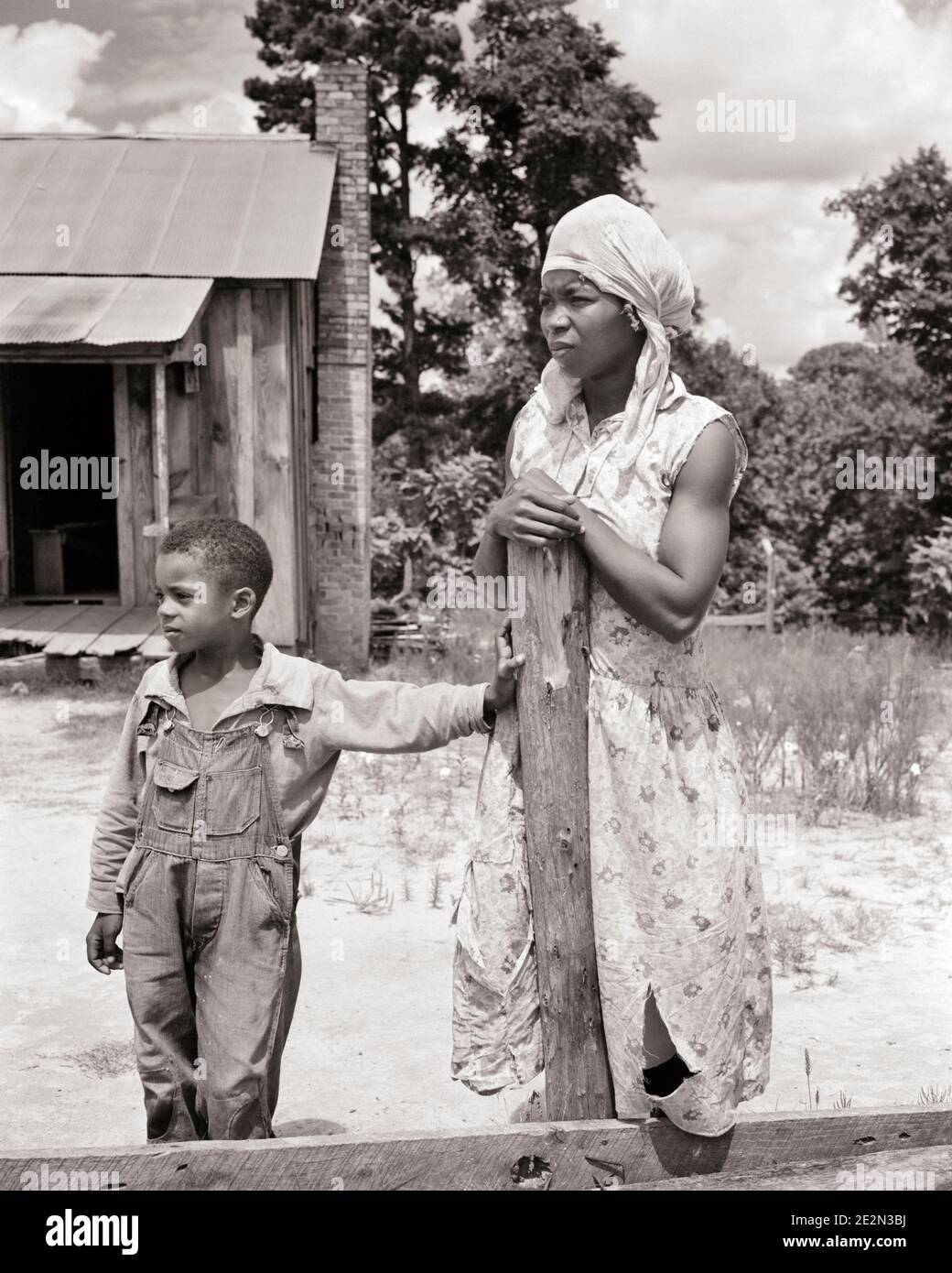 1930s AFRICAN-AMERICAN WOMAN MOTHER AND HER SON BOY STANDING BEFORE HOUSE BUILDING LEANING ON FARM FENCE POST ALABAMA USA - n73 HAR001 HARS LEANING OLD FASHION POVERTY 1 JUVENILE STYLE FEAR YOUNG ADULT SONS FAMILIES LIFESTYLE ARCHITECTURE FEMALES POOR RURAL HOME LIFE COPY SPACE HALF-LENGTH LADIES PERSONS FARMING MALES ALABAMA BUILDINGS AGRICULTURE B&W FREEDOM BEFORE DREAMS PROPERTY STRENGTH AFRICAN-AMERICANS AFRICAN-AMERICAN AND FARMERS SOUTHEAST BLACK ETHNICITY SOUTHERN REAL ESTATE CONNECTION CONCEPTUAL STRUCTURES RAGGED DISADVANTAGED EDIFICE DISAFFECTED DISAPPOINTED DISCONNECTED IMPOVERISHED Stock Photo