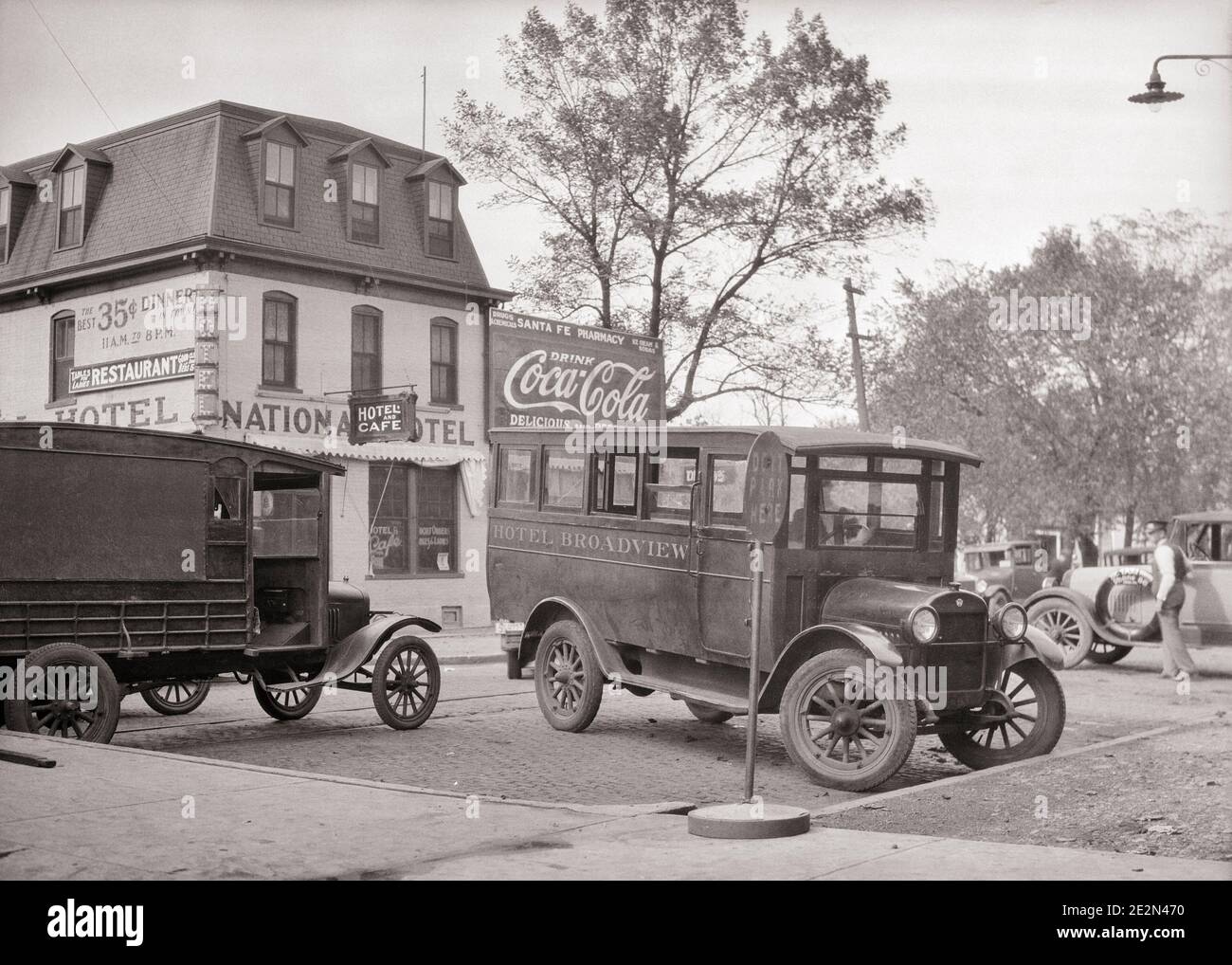 1920s MOTOR BUS AND DELIVERY VAN TRUCK PARKED WAITING AT RAILWAY RAILROAD STATION FOR PASSENGERS AND FREIGHT EMPORIA KANSAS USA  - q45713 CPC001 HARS BUILDINGS TRANSPORTATION B&W FREIGHT PARKED NORTH AMERICA NORTH AMERICAN STRUCTURE PROPERTY KS CUSTOMER SERVICE MOTOR VEHICLE AND EXTERIOR AT COCA-COLA REAL ESTATE STRUCTURES MANSARD ROOF EDIFICE EMPORIA BUSES TRANSIT BLACK AND WHITE MIDWEST MOTOR VEHICLES OLD FASHIONED Stock Photo