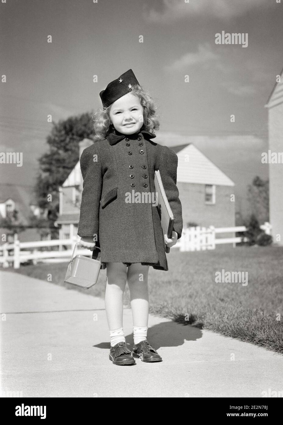1940s SMILING LITTLE GIRL READY FOR SCHOOL STANDING ON SIDEWALK WEARING BLACK HAT DOUBLE BREASTED COAT HOLDING LUNCH BOX & BOOK - s9722 HAR001 HARS COPY SPACE FULL-LENGTH B&W EYE CONTACT HAPPINESS CHEERFUL STYLES EXTERIOR POSING SMILES JOYFUL STYLISH PLEASANT AGREEABLE BREASTED CHARMING FASHIONS LOVABLE PLEASING ADORABLE APPEALING BLACK AND WHITE CAUCASIAN ETHNICITY HAR001 OLD FASHIONED Stock Photo