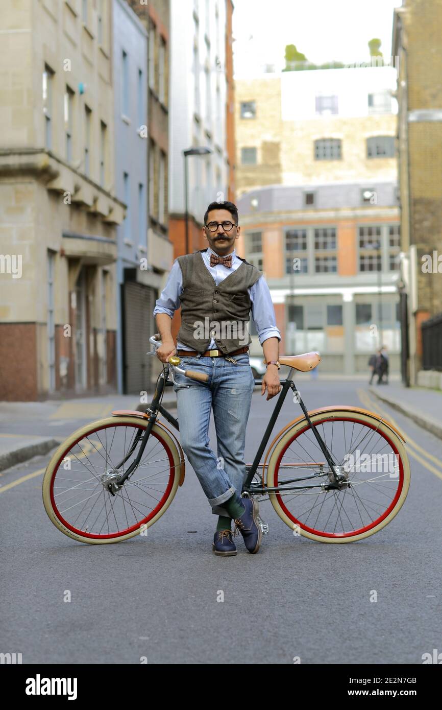 Asian man with bow tie and bicycle against wall Stock Photo