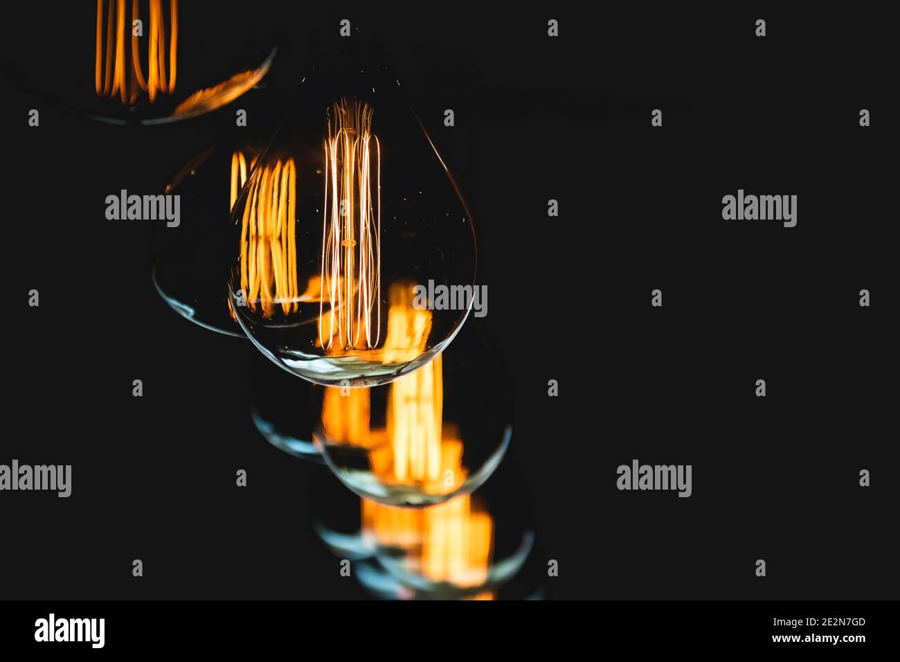 Lightbulb(s) and their glowing filaments shot in a dark interior of an upscale modern western-style saloon.  Orange and yellow glowing tones. Stock Photo