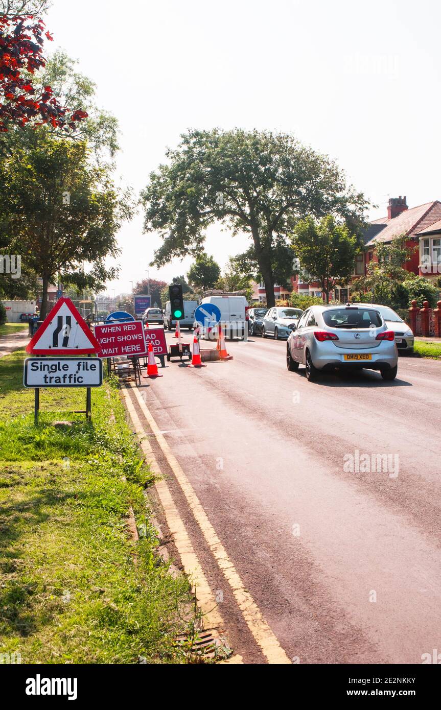 Cars going through road works with road narrows & lane indicator signs with single lane traffic controlled by traffic lights on green Stock Photo