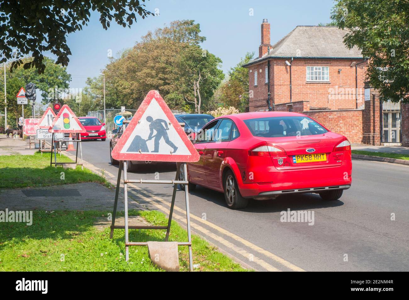 Cars waiting at road works with traffic warning & lane indicator signs with single lane traffic controlled by traffic lights on red Stock Photo