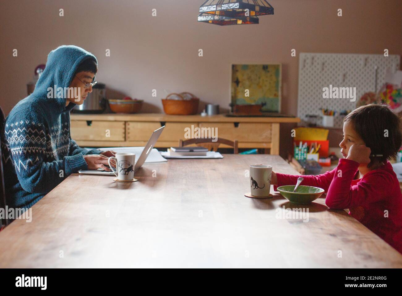 A father working on computer and child eating breakfast sit together Stock Photo