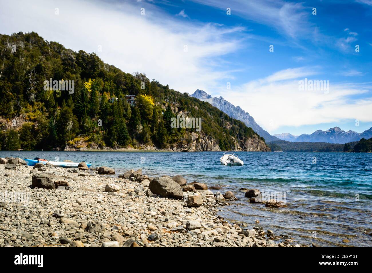 Lake shore with rocks, mountains and pine trees. A motorboat floating near a buoy. Summer in Bariloche. Stock Photo