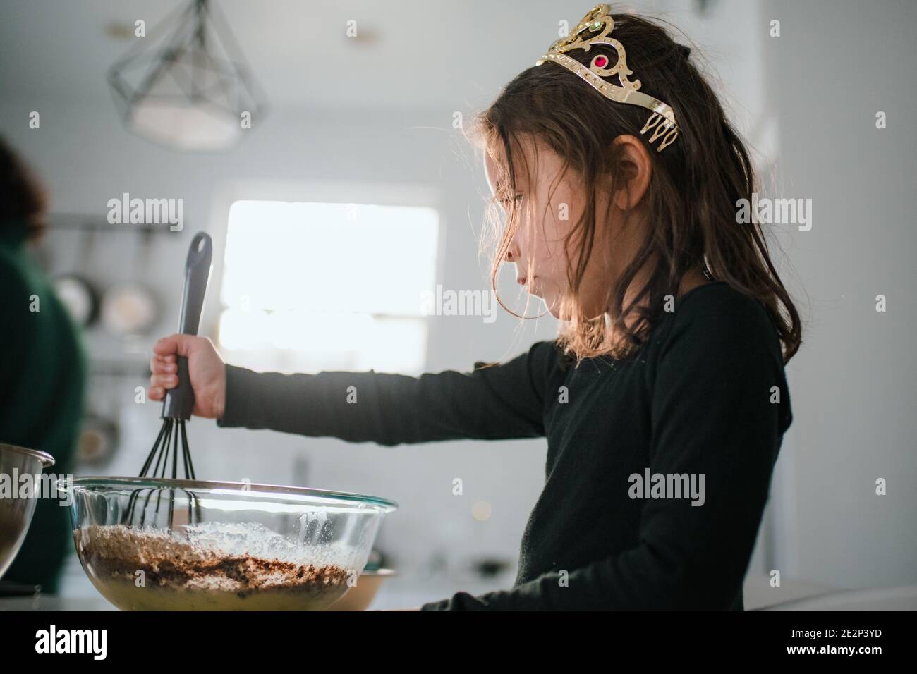 Preschool age girl in tiara baking with mixing bowl and whisk Stock Photo