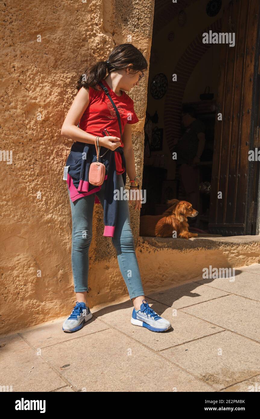 Little girl looking at cute dog standing in open door at Caceres. A fully preserved medieval town in Spain. Stock Photo