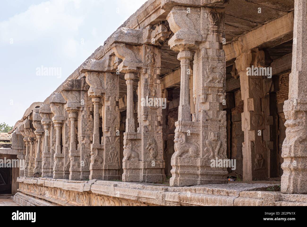 Hampi, Karnataka, India - November 5, 2013: Vijaya Vitthala Temple. Beige stone row of sculpted pillars along wall under light blue sky. Narasimha fre Stock Photo