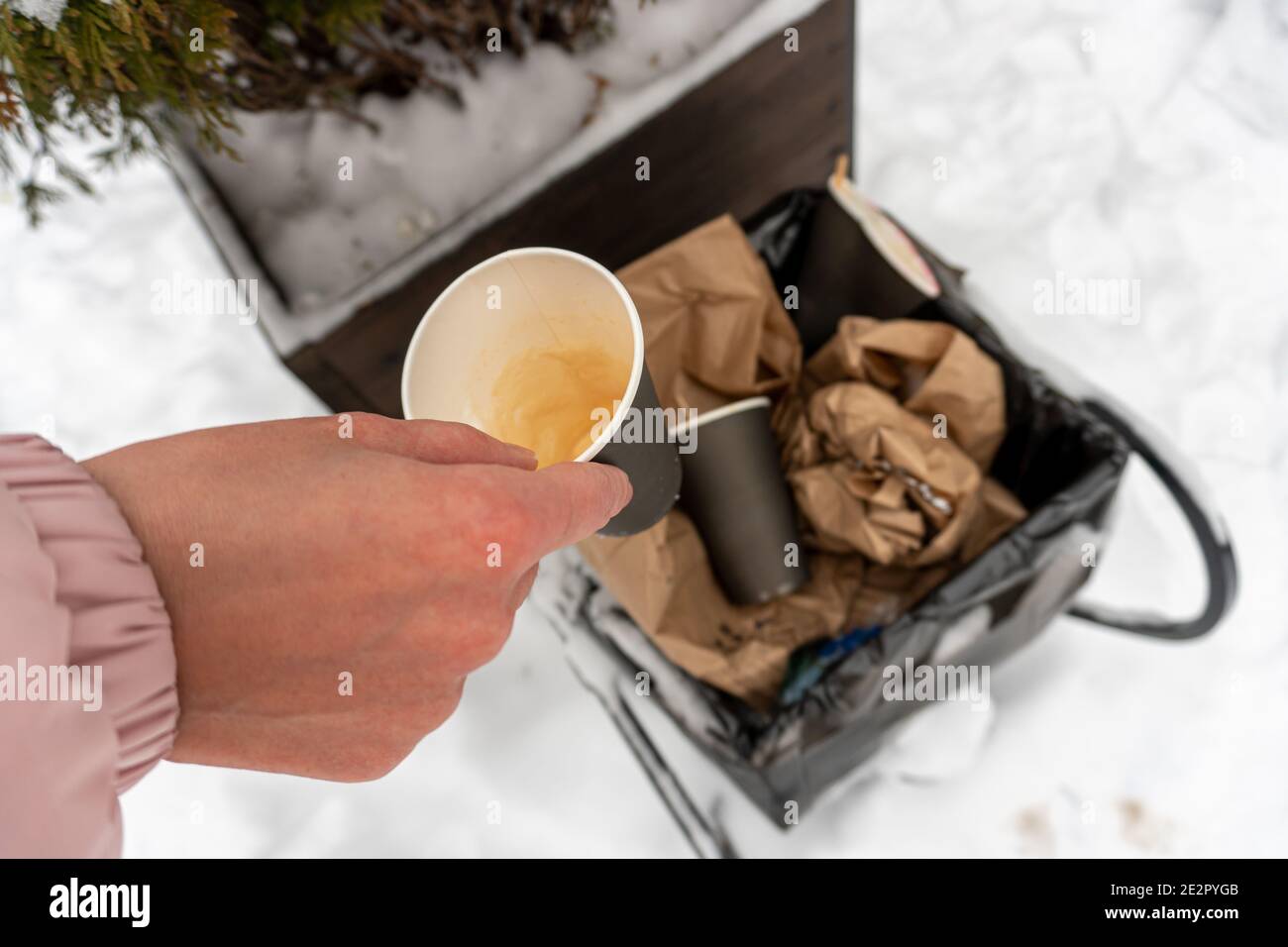 Girl throws a used coffee paper cup into the trash can near a cafe in winter Stock Photo