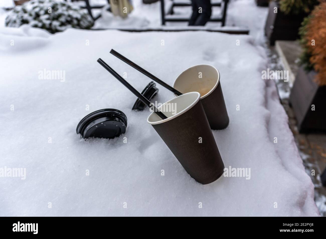 Two coffee cups and straws stick out in the snow on the terrace next to the street cafe Stock Photo