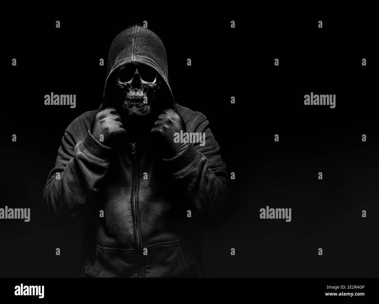 Horror photo of a scary man in hoodie with skull face on black background. Stock Photo