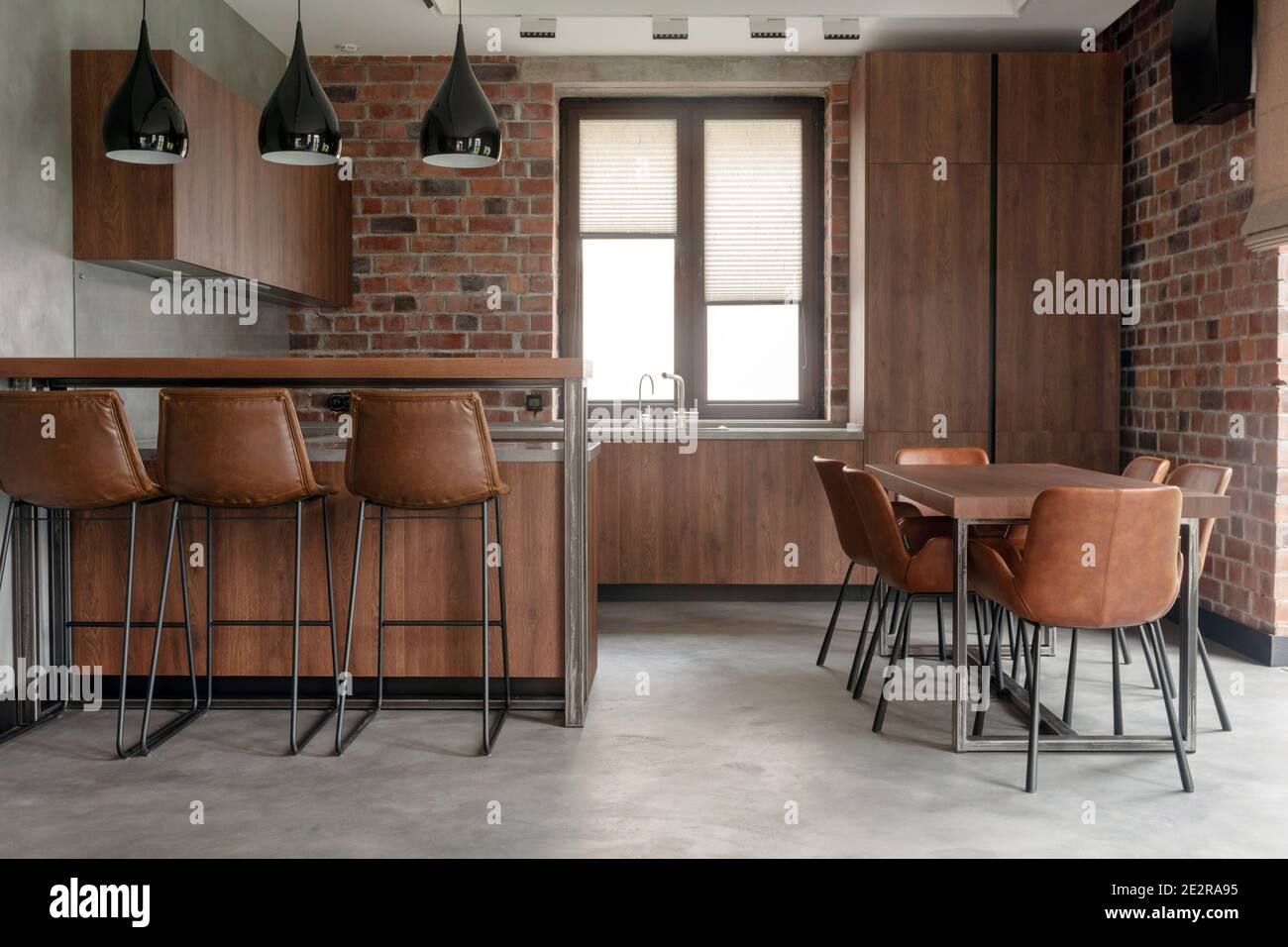 Contemporary interior design of light spacious dinning room including brown wooden furniture with bar stools at counter and soft comfortable chairs at Stock Photo