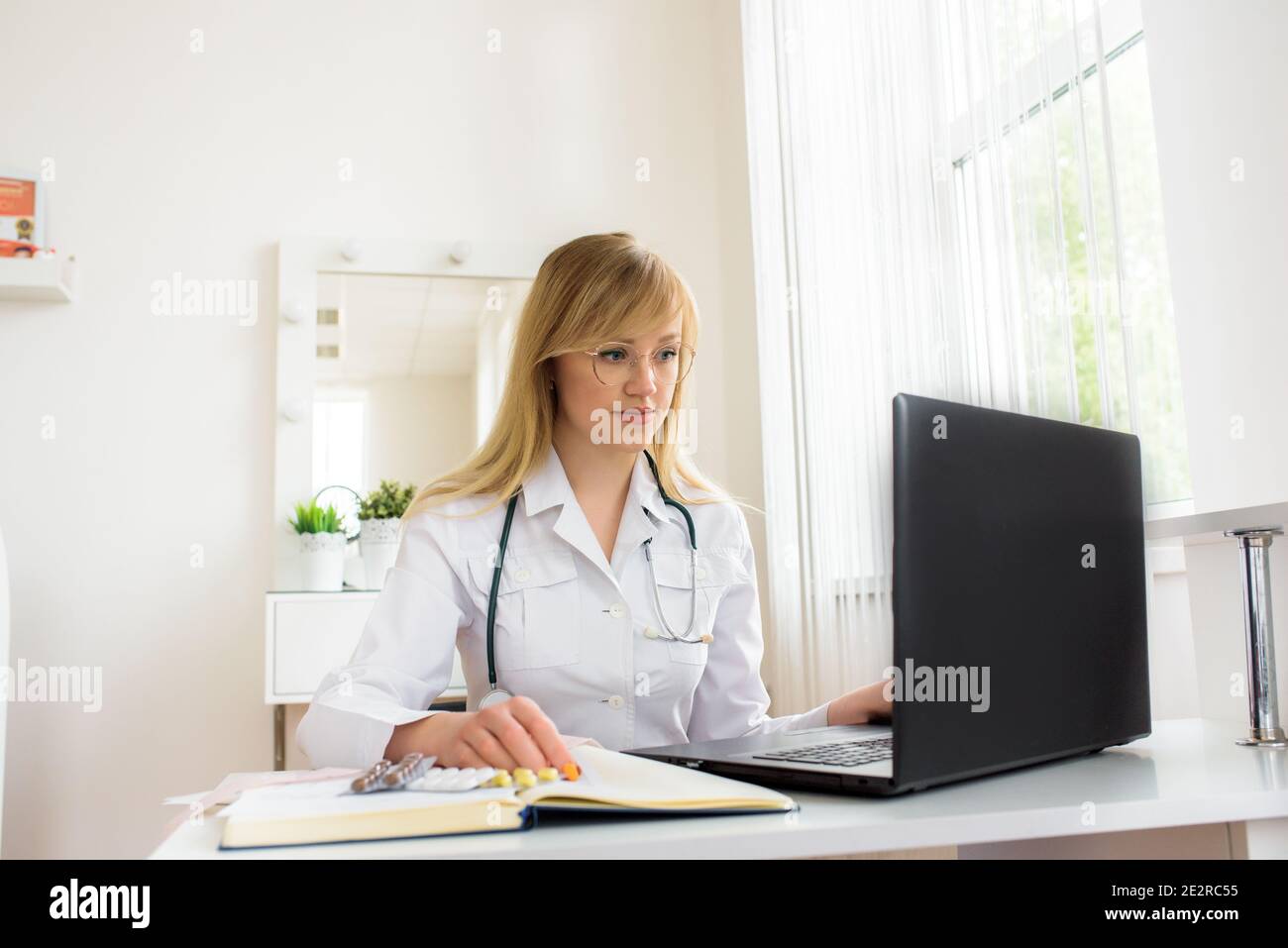 Online doctor consultation.Confident female doctor sitting at office desk and smiling at camera, health care and prevention concept Stock Photo