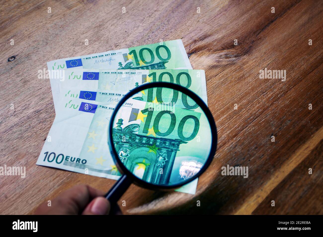 Magnification with a magnifying glass of the value of one of the hundred euro bills that are on a wooden surface Stock Photo