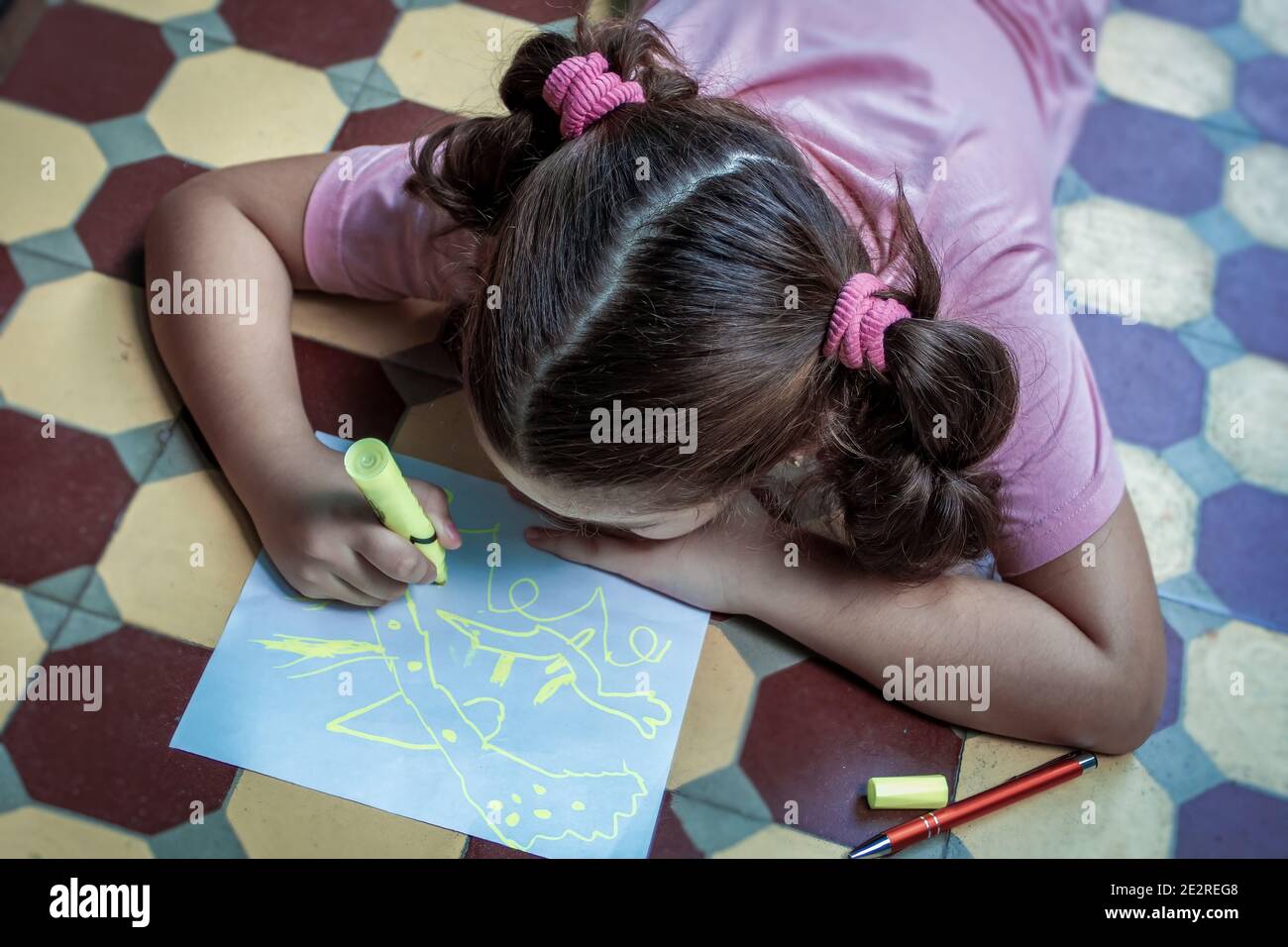 Little girl lying on the floor drawing on a sheet of paper with a ...