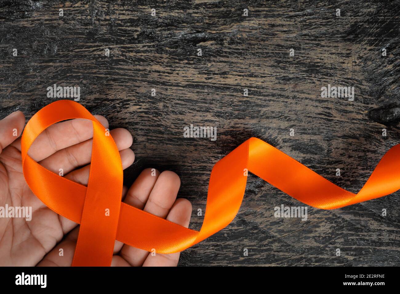 Top view of male hand holding orange ribbon on dark wood background