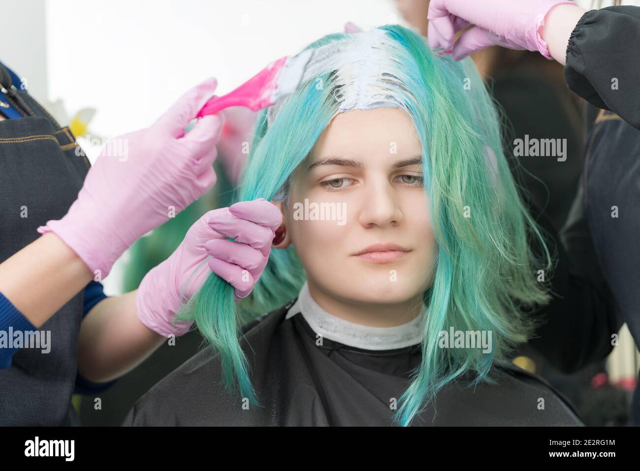 Process of bleaching hair roots in hair salon. Two hairdressers in protective glove use pink