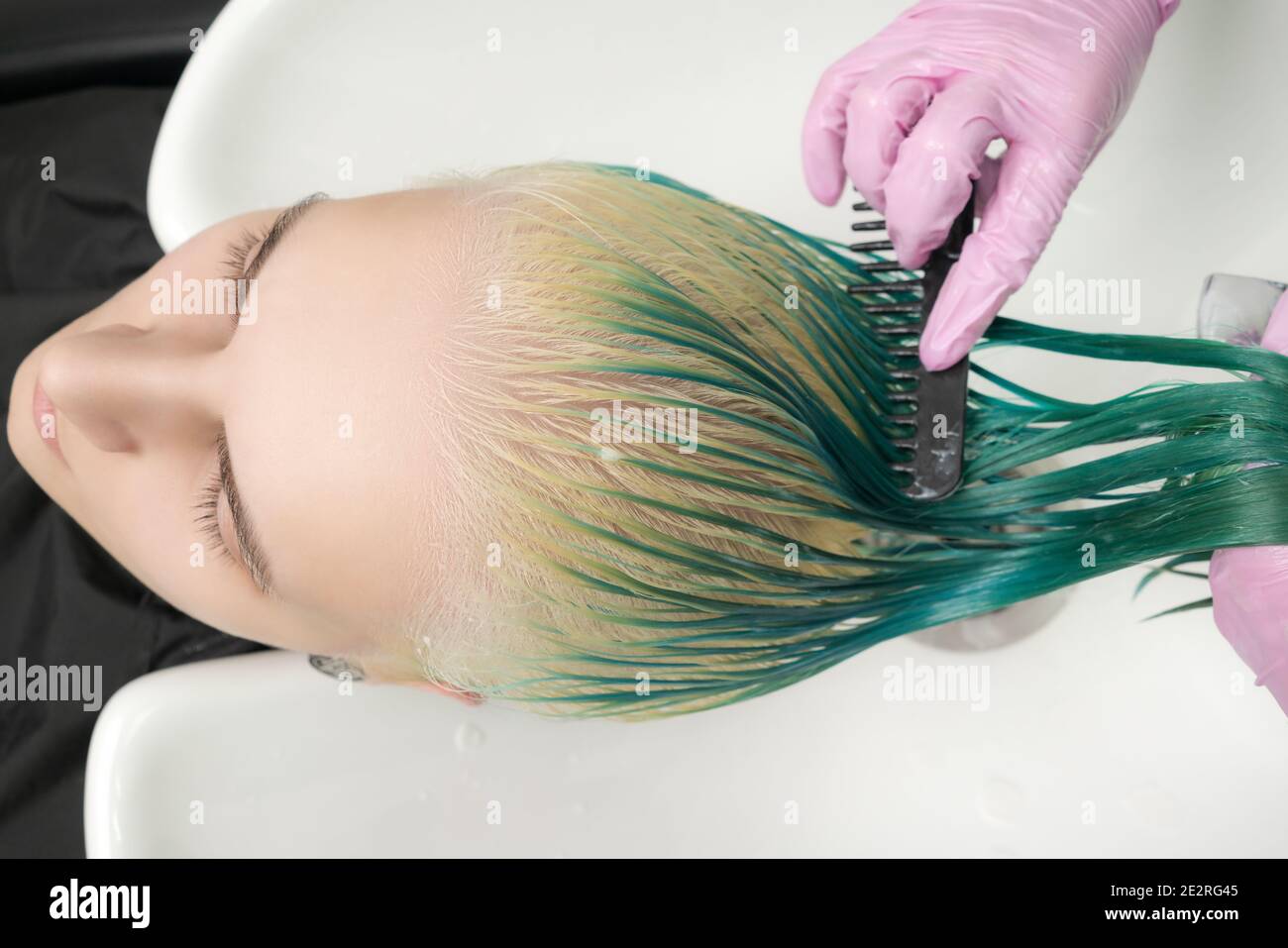 Top view of hairstylist holds wet hair in hand, combs long green and