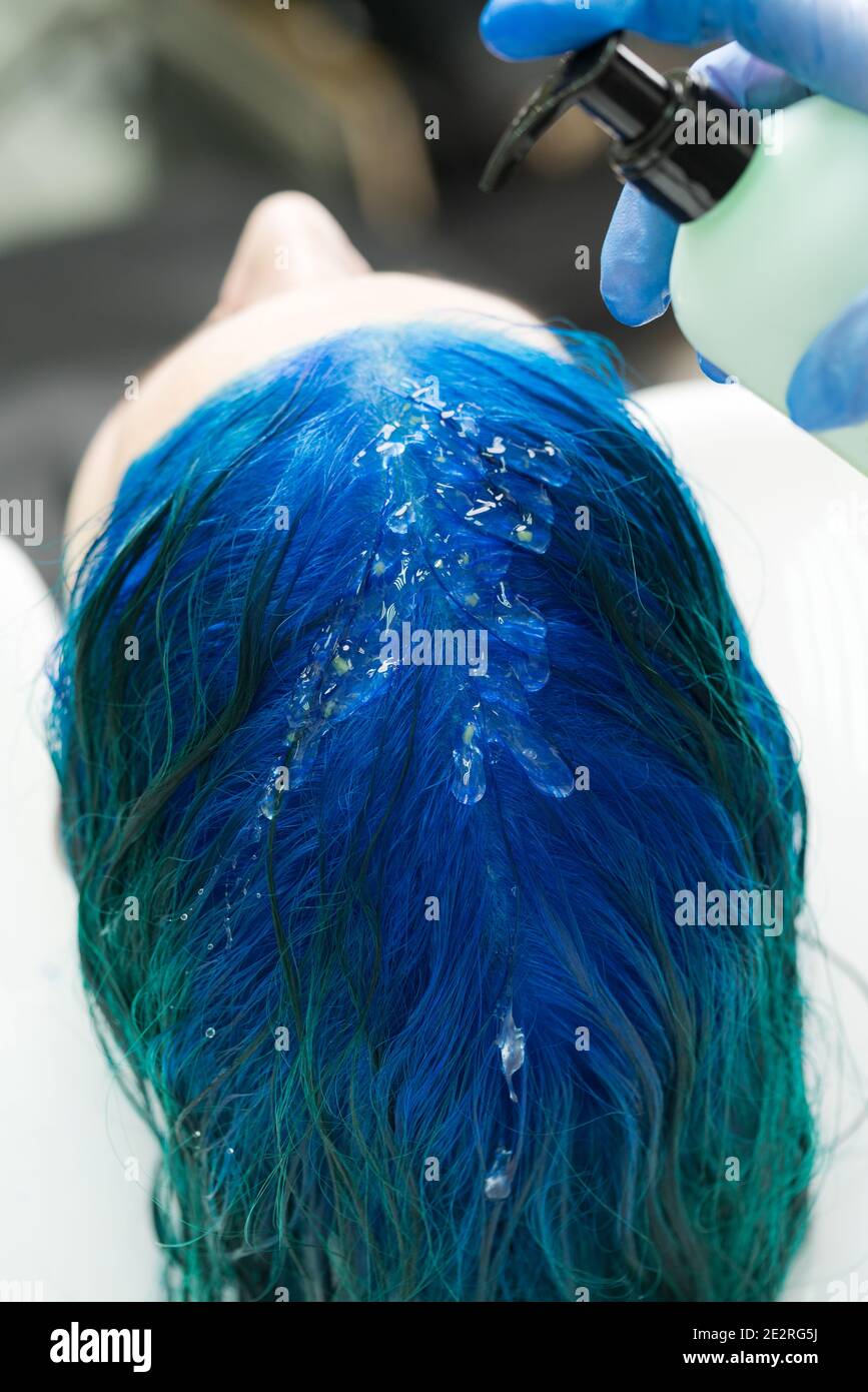 Professional hairdresser applies shampoo to client's blue hair for washing after process of coloring hair in dark blue color. Stock Photo