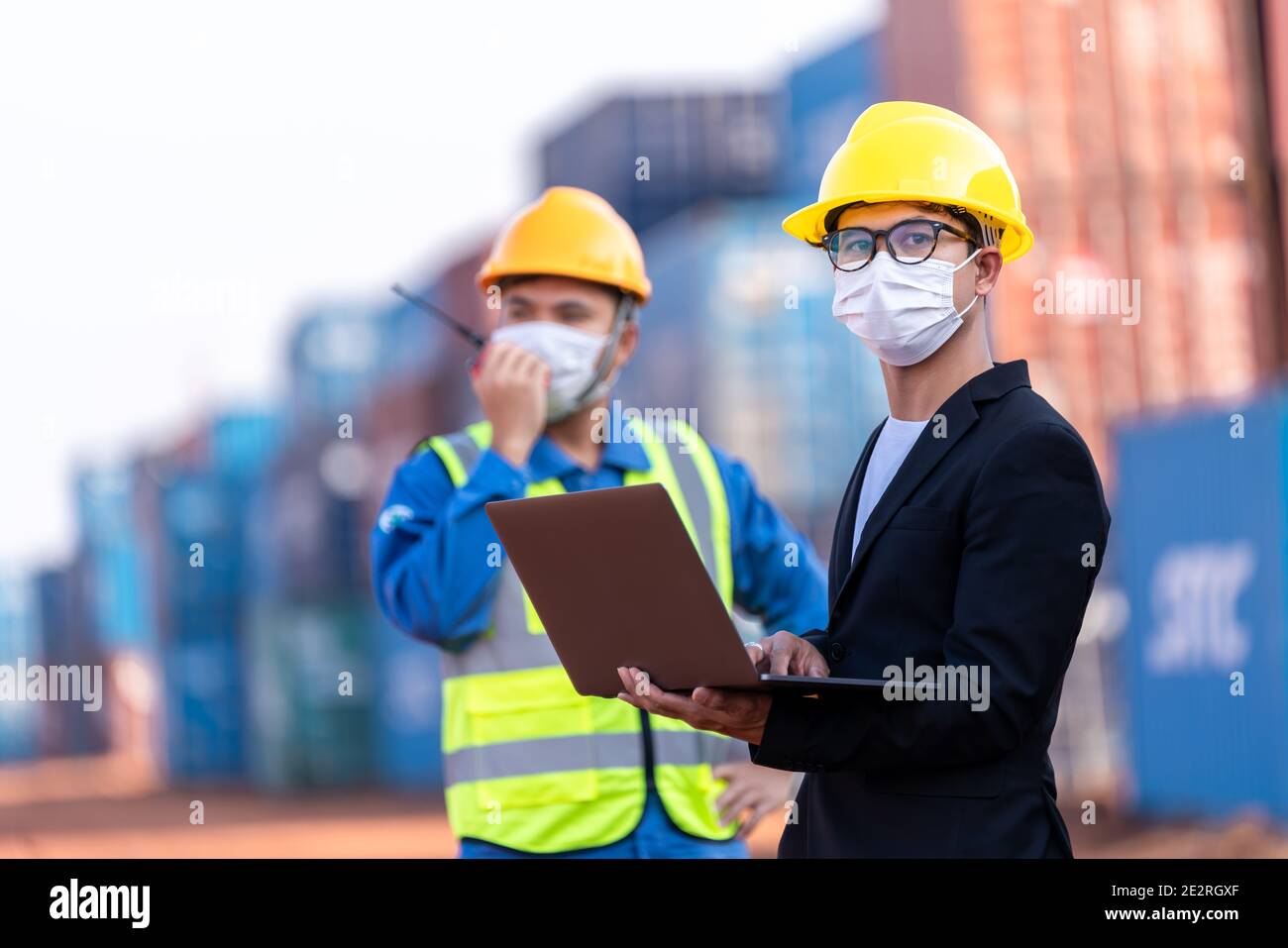 Asian male logistic warehouse foreman with worker using laptop checking list planning and strategy of container boxes from cargo freight ship. industr Stock Photo