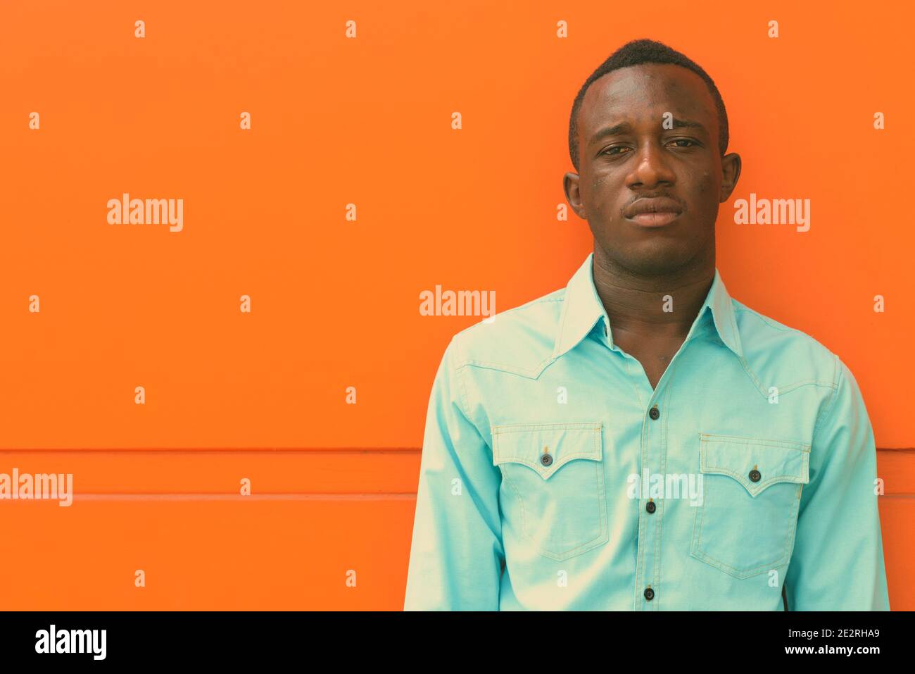 Young black African man leaning against orange painted wall Stock Photo