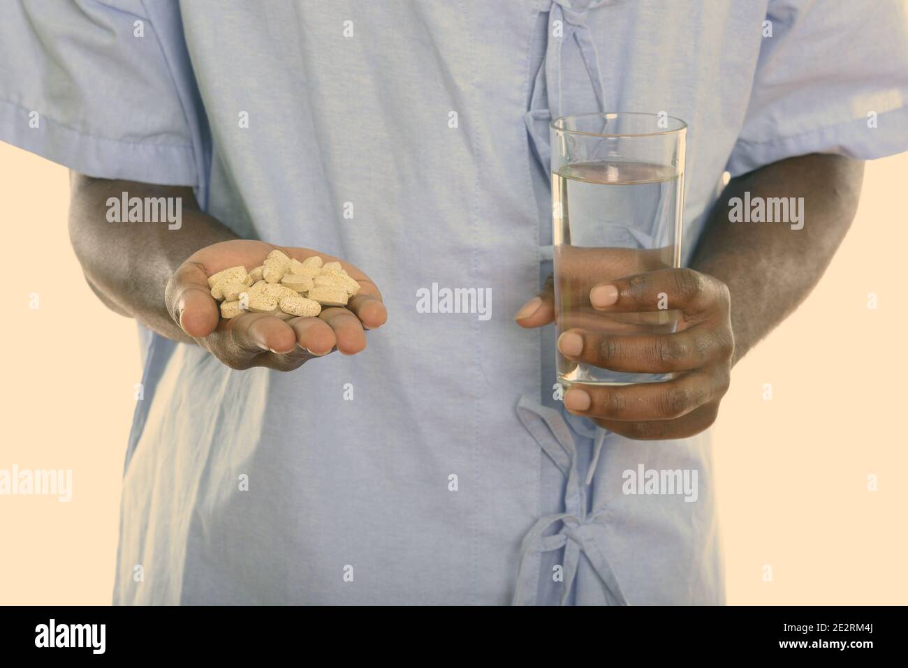 Studio shot of hands of young black African man patient holding vitamin tablets and glass of water Stock Photo