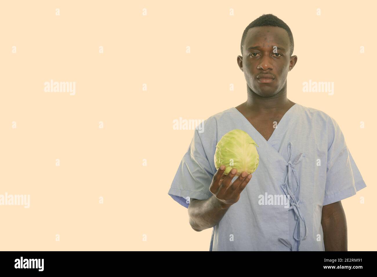 Studio shot of young black African man patient holding green cabbage