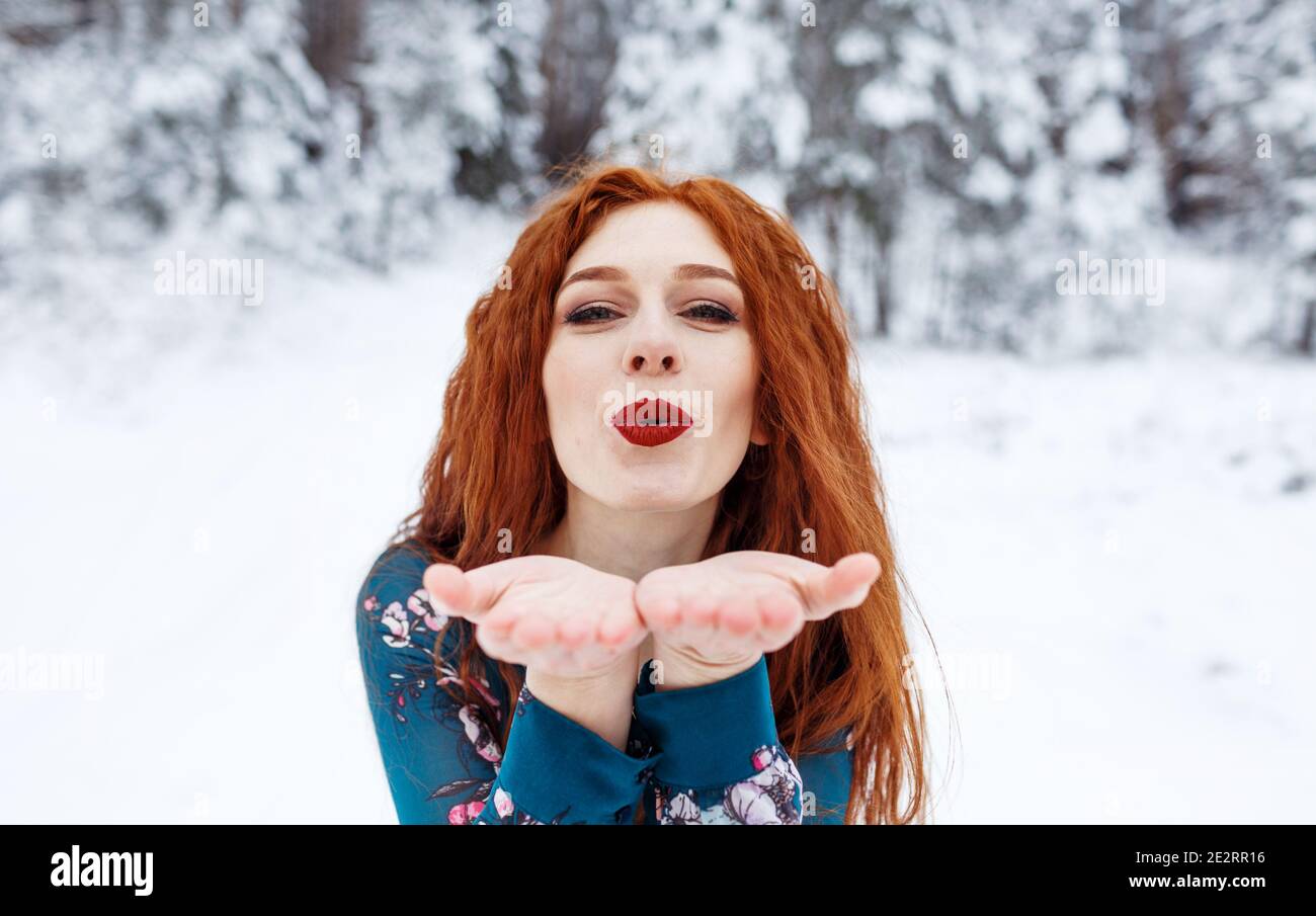 Young red-haired girl with long red hair on a winter background.Air kiss.  Red-haired woman in a summer dress on the background of winter nature Stock  Photo - Alamy