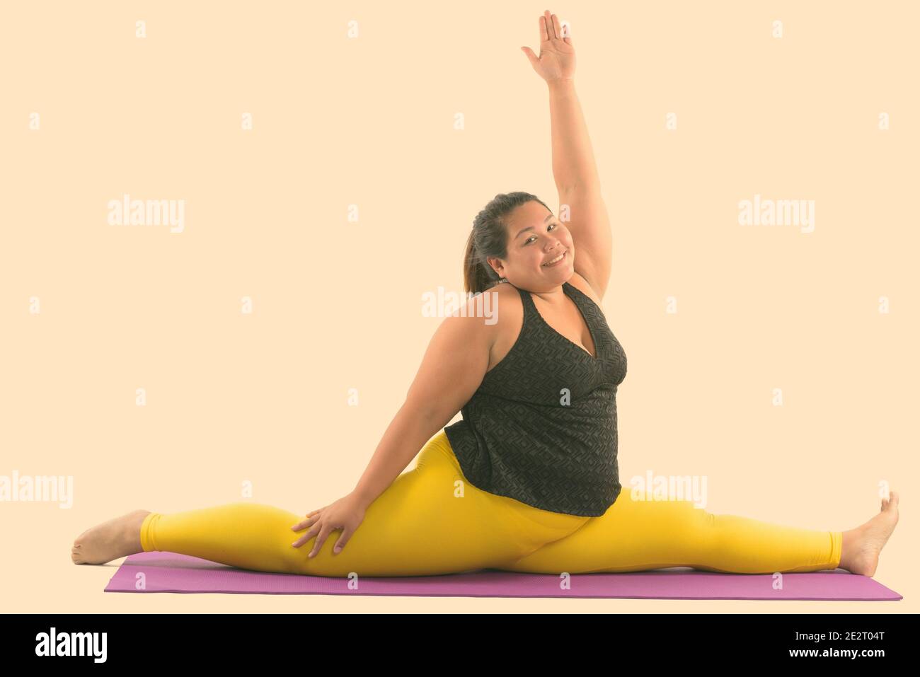 Studio shot of young happy fat Asian woman smiling and spitting her legs while reaching up Stock Photo